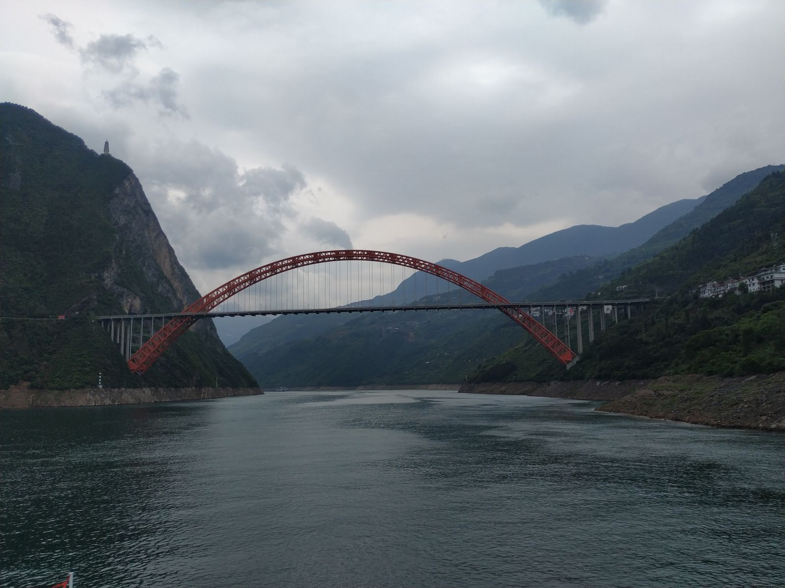 A red arch bridge spanning a mountain gorge on the Yangtze under a cloudy sky
